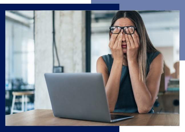 Person sitting at a laptop with their hands over their face showing frustration