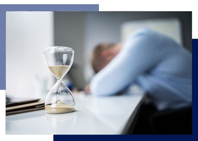 person with head down on laptop, with sand timer in foreground